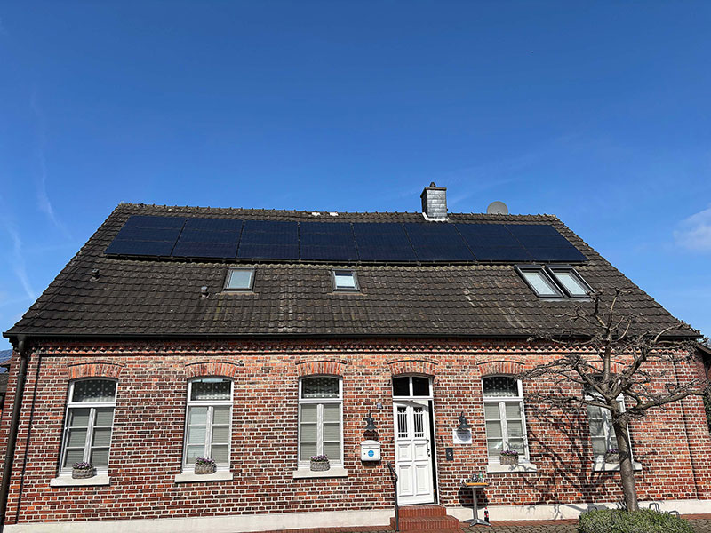 Ein Backsteinhaus mit einem weißen Eingang, mehreren Fenstern und solarbetriebenen Paneelen auf dem Dach unter einem klar blauen Himmel.
