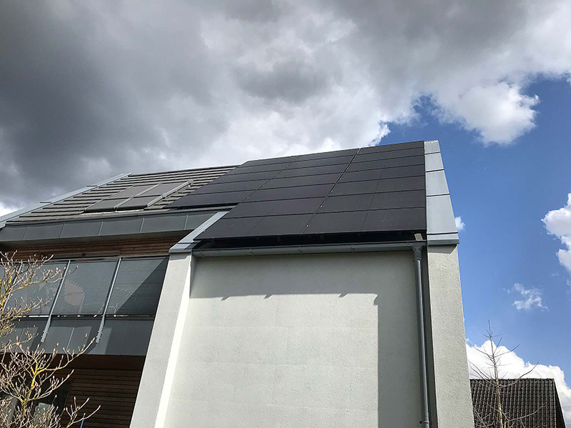 Modernes Haus mit einer Dachhälfte, die mit schwarzen Solarpaneelen bedeckt ist, unter einem bewölkten Himmel.