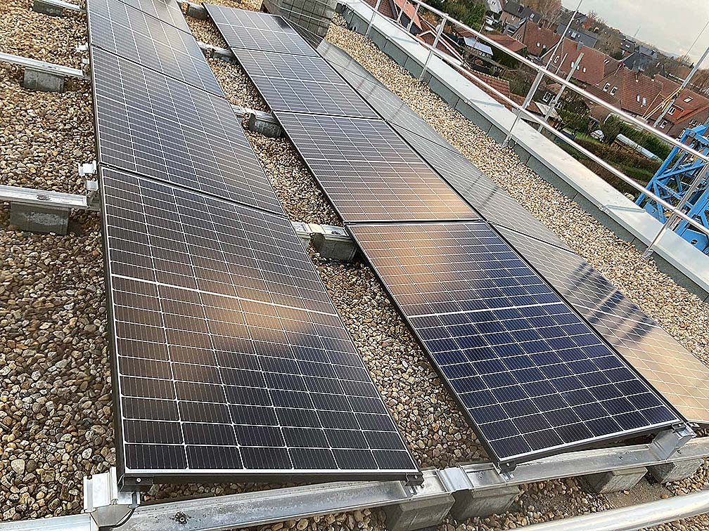 Drei Reihen von Solarpaneelen auf einem Schotterflachdach mit Hausdächern im Hintergrund.