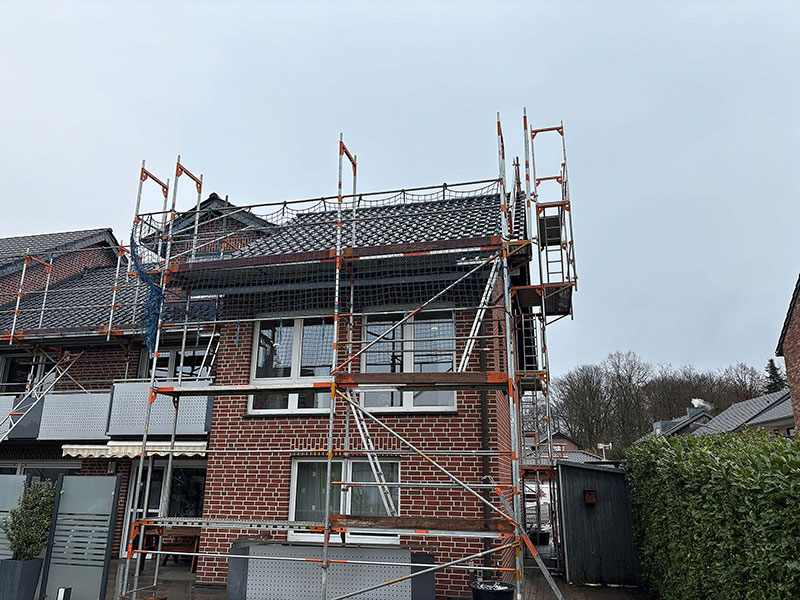 Backsteinhaus mit Gerüst für Bau- oder Renovierungsarbeiten unter bewölktem Himmel.