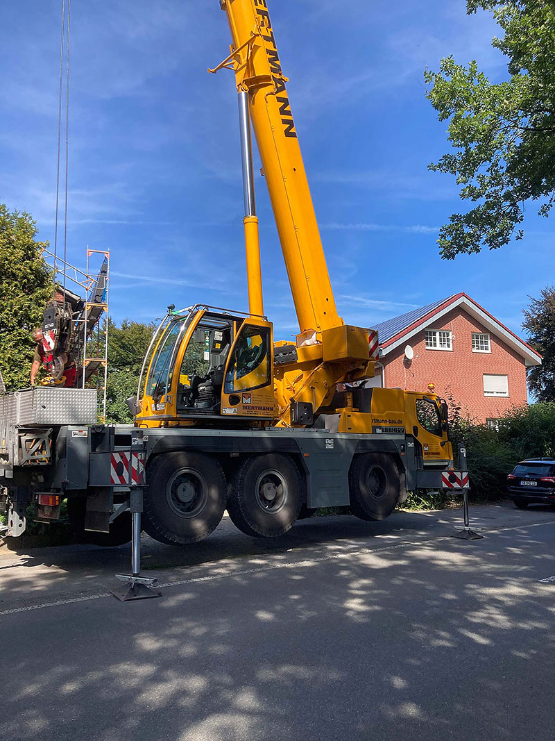 Gelber mobiler Kran mit ausgefahrenen Stützen steht auf einer Straße vor Wohnhäusern an einem sonnigen Tag.